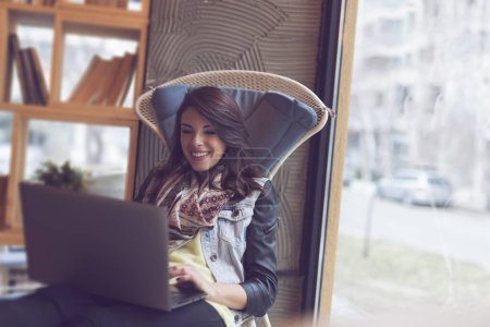 Téléchargez les photos : Belle jeune femme assise dans un café et travaillant sur un ordinateur portable - en image libre de droit