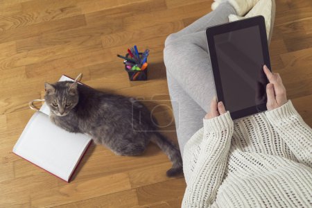 Téléchargez les photos : Vue de dessus d'une femme assise sur le sol, tenant une tablette et travaillant à la maison avec un planificateur et un assistant chat. Concentration sélective - en image libre de droit
