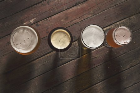 Téléchargez les photos : Vue de dessus d'une bière pâle, foncée, non filtrée et aux fruits rouges dans quatre verres à bière différents sur une table en bois rustique - en image libre de droit