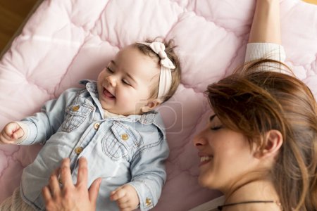 Foto de Vista superior de una madre y su adorable bebé acostado en la cama en el dormitorio, sonriendo y jugando. Concéntrate en el bebé - Imagen libre de derechos