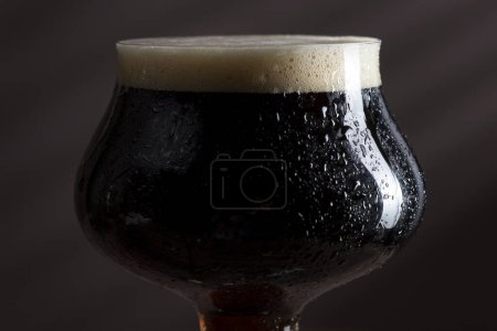 Photo for Close up of a wet glass of cold dark beer with foam. Selective focus - Royalty Free Image