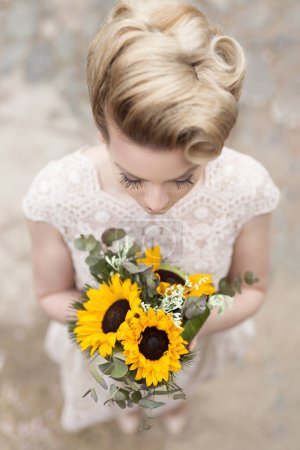 Téléchargez les photos : Vue de dessus d'une belle jeune mariée dans une robe de mariée, debout sur une route pavée et tenant un bouquet de tournesol - en image libre de droit