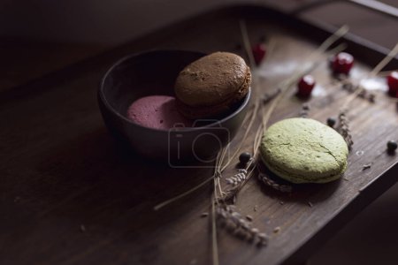 Foto de Vista superior de las galletas de macaron en una bandeja de madera, con un tazón, fruta de cereza y flores de lavanda colocadas junto a ella. Enfoque selectivo - Imagen libre de derechos