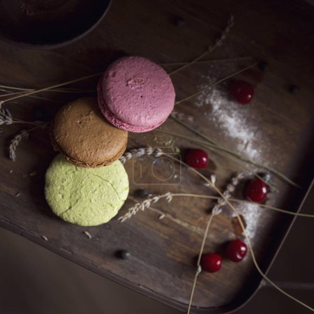 Photo for Top view of macaron cookies on a wooden tray, with cherry fruit and lavender flowers placed next to it. Selective focus - Royalty Free Image