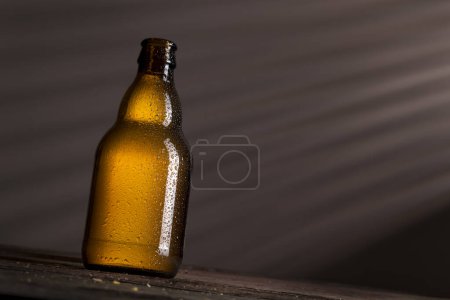 Foto de Botella de cerveza húmeda bien refrigerada colocada en una mesa de madera rústica en un bar - Imagen libre de derechos