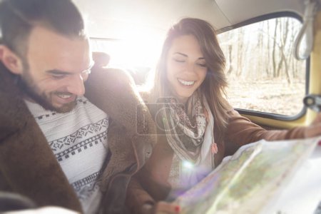 Téléchargez les photos : Jeune couple assis dans une vieille voiture, lisant une carte, à la recherche d'un itinéraire pour leur voyage sur la route - en image libre de droit