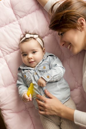 Photo for Top view of a mother and her adorable baby girl lying on the bed in bedroom, smiling and playing. Focus on the baby - Royalty Free Image