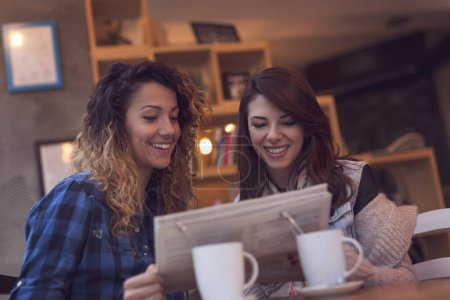 Foto de Dos chicas sentadas en un café, bebiendo café de la mañana y leyendo periódicos. Concéntrate en la chica de la derecha - Imagen libre de derechos