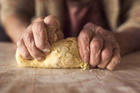 Photo for Detail of an elderly woman's hand kneading dough while making homemade pasta. Selective focus on the hand and dough - Royalty Free Image