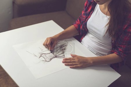 Photo for Detail of young fashion designer making a sketch of a new dress design. Focus on the charcoal in her hand - Royalty Free Image