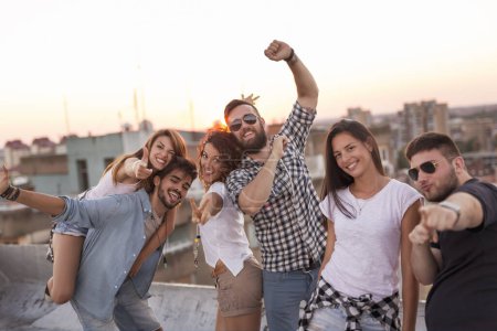 Foto de Grupo de jóvenes divirtiéndose en una fiesta de verano en la azotea, al atardecer. Concéntrate en la pareja en el medio - Imagen libre de derechos