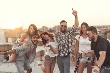 Téléchargez les photos : Groupe de jeunes qui s'amusent lors d'une fête sur le toit en été, au coucher du soleil. Concentrez-vous sur les gens au milieu - en image libre de droit