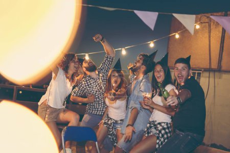 Foto de Grupo de jóvenes amigos celebrando una fiesta de cumpleaños en la azotea de un edificio, bailando y divirtiéndose - Imagen libre de derechos