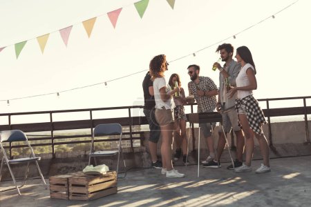 Photo for Group of young friends having fun at rooftop party, making barbecue and enjoying hot summer days. Focus on the guy in the middle - Royalty Free Image