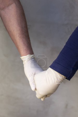 Foto de Detalle de pareja con guantes médicos de protección tomados de la mano como parte de la protección contra el coronavirus y la prevención del campagne; amor en tiempo de pandemia covid-19 - Imagen libre de derechos