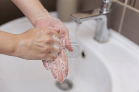Photo for Woman washing and disinfecting hands with soap and hot water as part of coronavirus prevention and protection protocols; stop spreading covid-19 hygiene protocols - Royalty Free Image