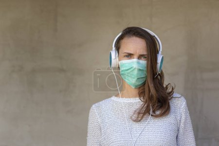 Photo for Portrait of a young woman wearing medical face protection mask as part of covid-19 prevention campaign, listening to the music and relaxing during pandemic - Royalty Free Image