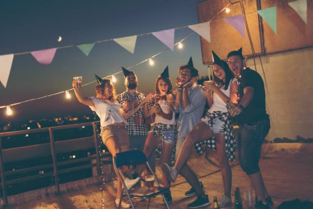 Téléchargez les photos : Groupe de jeunes amis ayant une fête d'anniversaire sur un toit du bâtiment, dansant et s'amusant - en image libre de droit