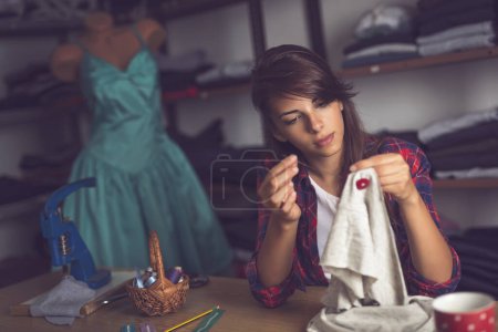 Photo for Young seamstress making some repairs, manually sewing in buttons on a shirt - Royalty Free Image