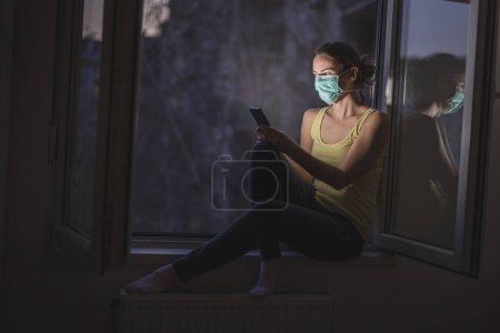 Photo for Woman wearing surgical medical face protection mask while in self isolation at home after having coronavirus infection symptoms; covid-19 home isolation - Royalty Free Image