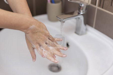 Photo for Woman washing and disinfecting hands with soap and hot water as part of coronavirus prevention and protection protocols; stop spreading covid-19 hygiene protocols - Royalty Free Image