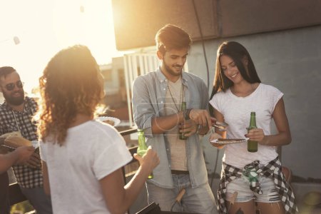 Téléchargez les photos : Groupe de jeunes amis s'amuser à la fête sur le toit, faire un barbecue et profiter des chaudes journées d'été. Focus sur le couple à côté du barbecue - en image libre de droit