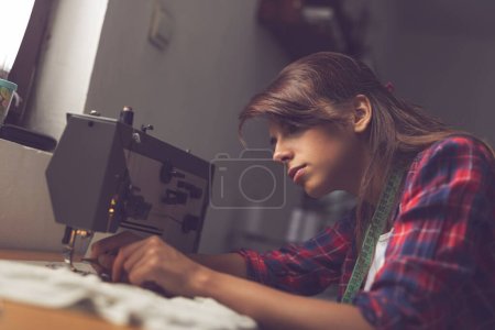 Foto de Trabajador de la industria textil joven tirando de la banda de rodadura en la aguja en una máquina de coser - Imagen libre de derechos