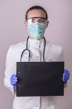 Photo for Detail of doctor in uniform wearing medical protective gloves holding blank paper holder writing board; medical staff in fight against covid-19 pandemic - Royalty Free Image