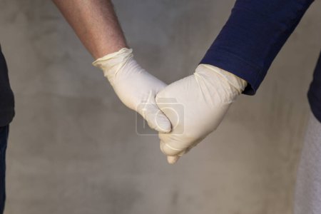 Foto de Detalle de pareja con guantes médicos de protección tomados de la mano como parte de la campaña de protección y prevención del coronavirus; amor en tiempo de pandemia covid-19 - Imagen libre de derechos
