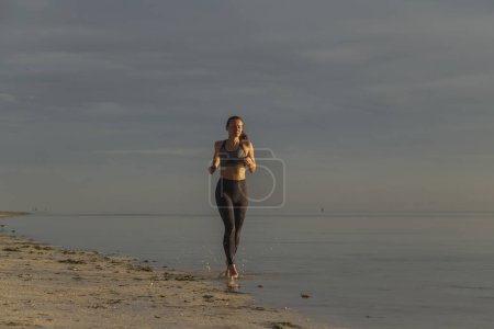Photo for Young woman working out on the beach in the morning, jogging along the coastline - Royalty Free Image