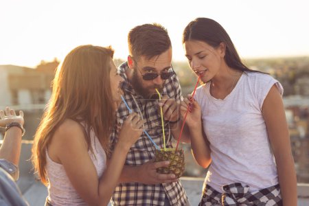 Téléchargez les photos : Groupe de jeunes amis s'amuser à la fête sur le toit, profiter d'un beau coucher de soleil sur la ville et boire un cocktail d'ananas - en image libre de droit