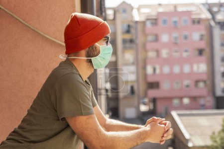 Photo for Portrait of a man wearing medical face protection mask while standing on a balcony in home isolation during covid-19 lockdown - Royalty Free Image