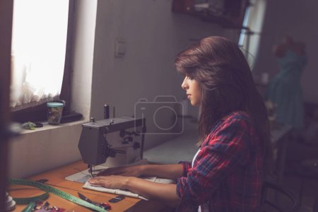 Téléchargez les photos : Couture assise à une machine à coudre et couture - en image libre de droit