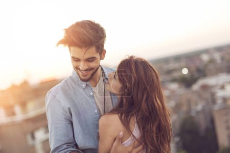 Téléchargez les photos : Couple amoureux debout sur le toit d'un immeuble, profitant d'un magnifique coucher de soleil sur les lignes de ski de la ville et câlins - en image libre de droit