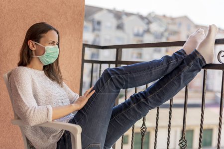 Foto de Mujer con máscara de protección facial médica al aire libre como parte de los protocolos de protección y prevención del coronavirus; mujer en el balcón durante el bloqueo de covid-19 - Imagen libre de derechos