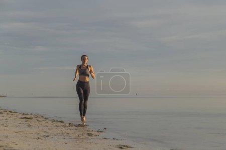 Photo for Young woman working out on the beach in the morning, running along the coastline - Royalty Free Image