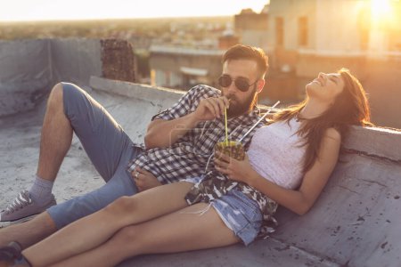 Foto de Pareja joven enamorada bebiendo un cóctel de piña y divirtiéndose en la fiesta de verano en la azotea al atardecer. - Imagen libre de derechos