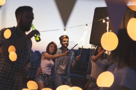 Photo for Group of young friends having fun at a rooftop party. Focus on the couple in the middle - Royalty Free Image