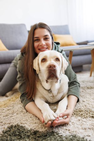 Téléchargez les photos : Belle jeune femme étreignant et câlinant son chien de compagnie tout en se relaxant et en appréciant le temps libre à la maison - en image libre de droit