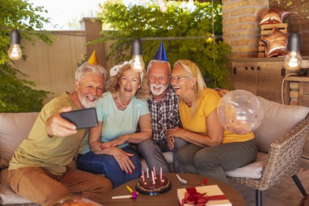 Foto de Grupo de alegres amigos mayores divirtiéndose en una fiesta de cumpleaños, tomando una selfie con pastel de cumpleaños - Imagen libre de derechos