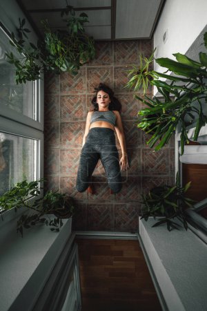 Téléchargez les photos : Vue en angle élevé de la jeune femme active en vêtements de sport faisant du yoga sur son balcon à la maison le matin - en image libre de droit