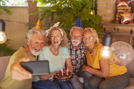 Photo for Group of cheerful elderly people having fun celebrating friend's birthday, taking a selfie with birthday cake while at the party - Royalty Free Image