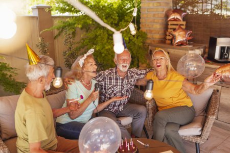Téléchargez les photos : Groupe de personnes âgées gaies ayant une fête d'anniversaire pour un ami, s'amusant à chanter karaoké - en image libre de droit