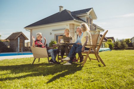 Photo for Group of cheerful senior friends having lunch in the backyard by the swimming pool, gathered around the table, eating, drinking and enjoying sunny summer day outdoors - Royalty Free Image