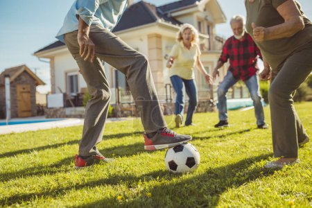 Foto de Detalle de personas mayores activas divirtiéndose jugando fútbol en el césped en el patio trasero, disfrutando de un soleado día de verano al aire libre - Imagen libre de derechos