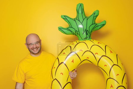 Foto de Hombre alegre sosteniendo flotador de natación inflable en forma de piña sobre fondo de color amarillo - vacaciones de verano y concepto de viaje - Imagen libre de derechos