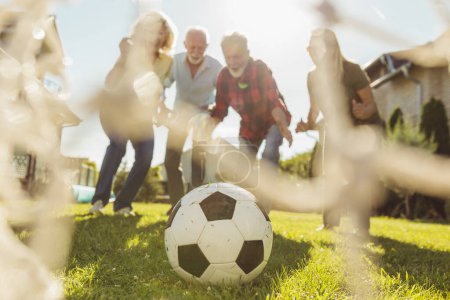 Foto de Grupo de personas mayores activas que se divierten jugando al fútbol en el césped en el patio trasero, disfrutando de un soleado día de verano al aire libre, celebrando después de marcar un gol - Imagen libre de derechos