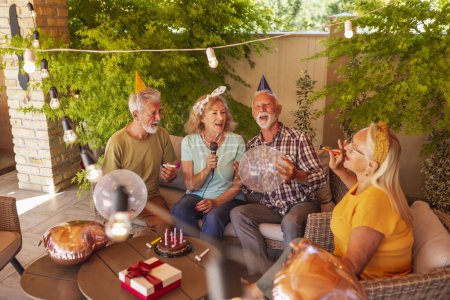 Foto de Grupo de personas mayores alegres divirtiéndose cantando karaoke en una fiesta de cumpleaños - Imagen libre de derechos