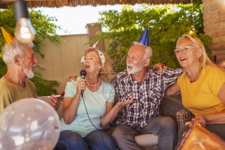 Foto de Grupo de personas mayores alegres tener una fiesta de cumpleaños para un amigo, divertirse cantando karaoke - Imagen libre de derechos