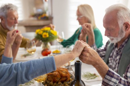 Foto de Grupo de personas mayores que celebran el Día de Acción de Gracias juntos en casa durante la cena tradicional, orando y expresando gratitud antes de la cena - Imagen libre de derechos
